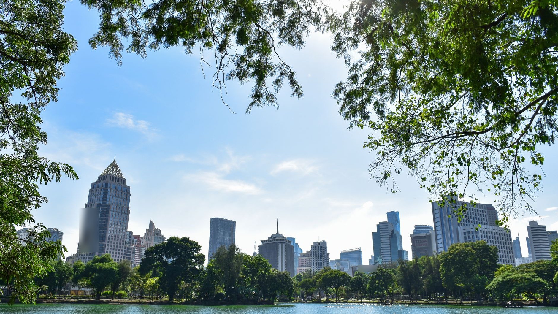 Bangkok high-rise towers seen across a lake and trees in a city park (illustrative stock photo)
