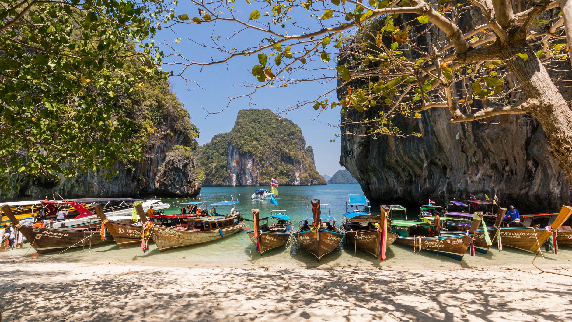 Longtail boats moored on a sandy Andaman Sea beach beneath limestone cliffs (illustrative stock photo)