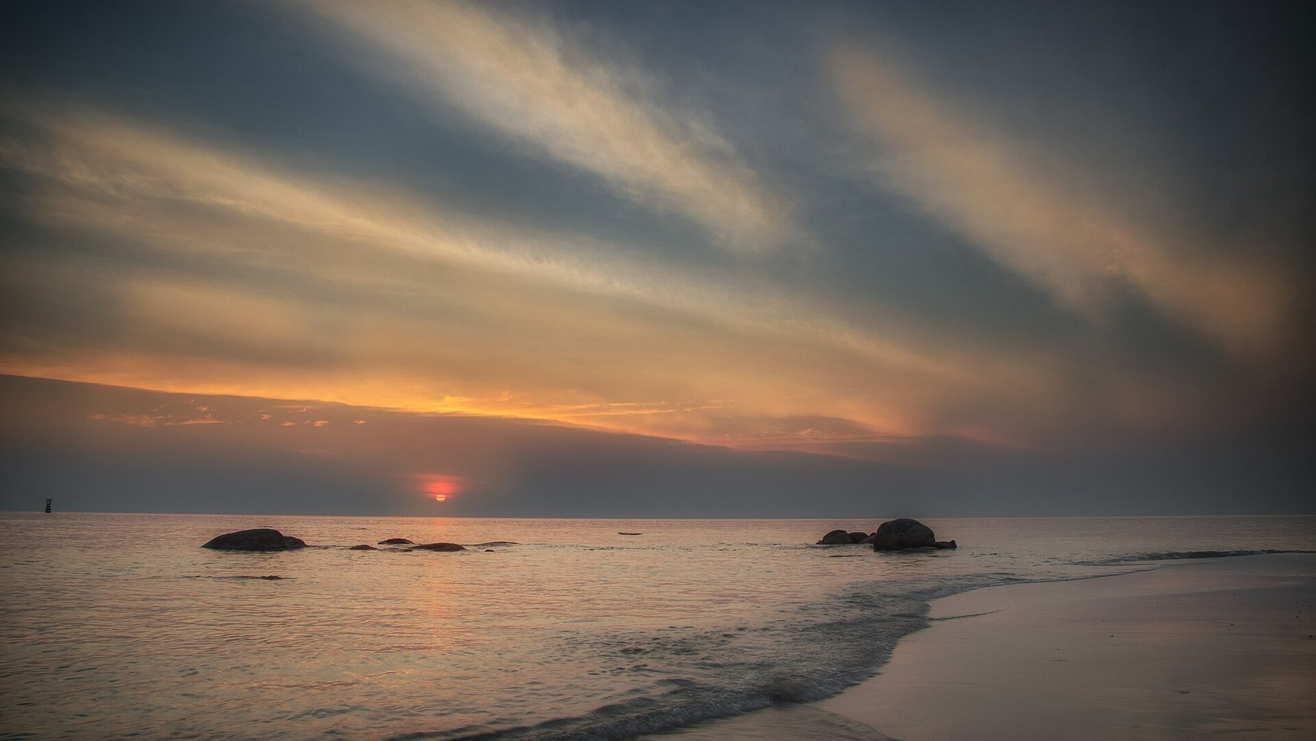 Sunrise over the Gulf of Thailand from the public beach at Hua Hin, with rocks in calm water (illustrative photo)