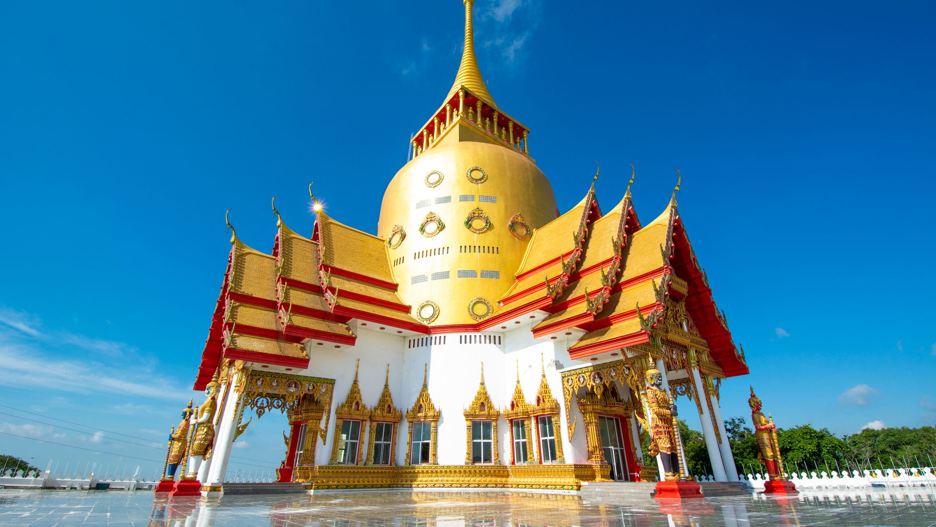 A gilded Thai Buddhist shrine with a golden spire and red-trimmed roofs under a blue sky (illustrative stock photo)