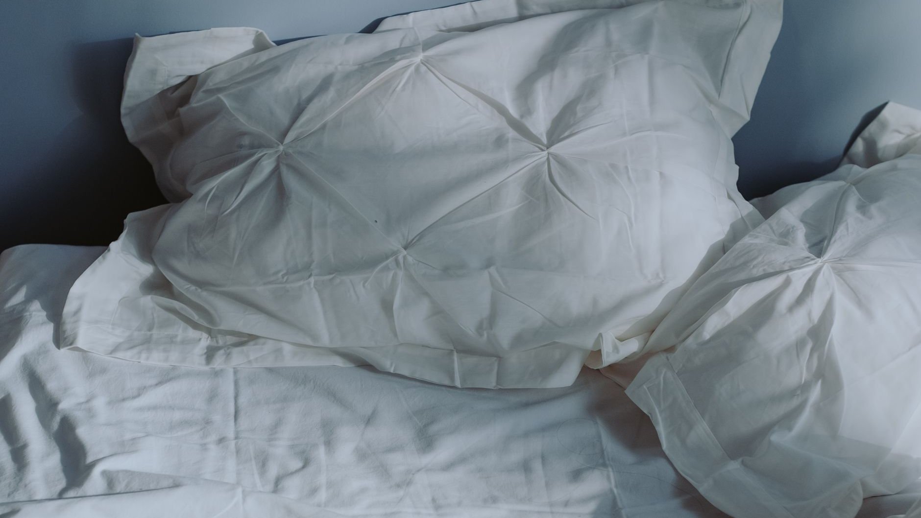 White pillows and bedding on a made bed in soft light (illustrative stock photo)