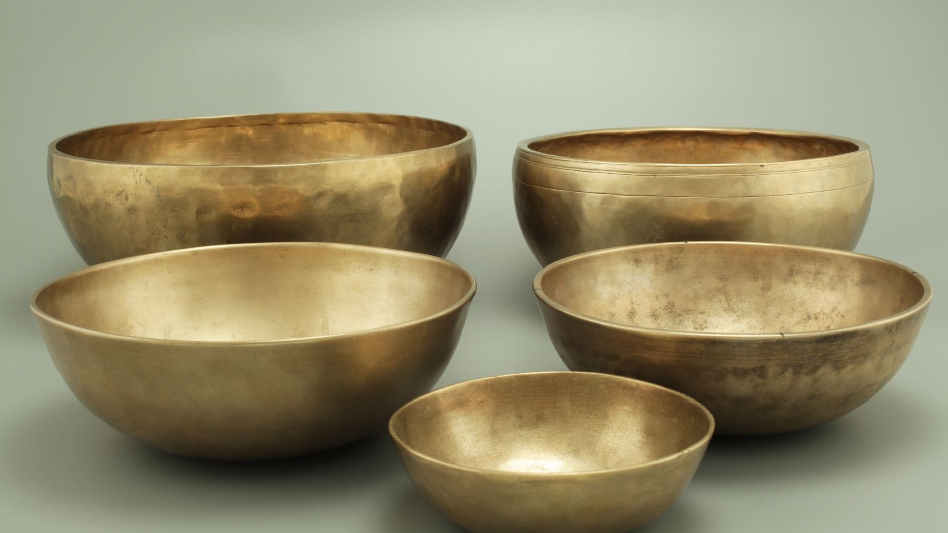Five antique brass singing bowls of different sizes on a plain grey background (illustrative stock photo)