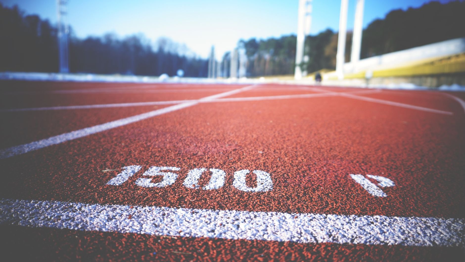 A red running track with white lane lines and a 1500 metre marking under a blue sky (illustrative stock photo)