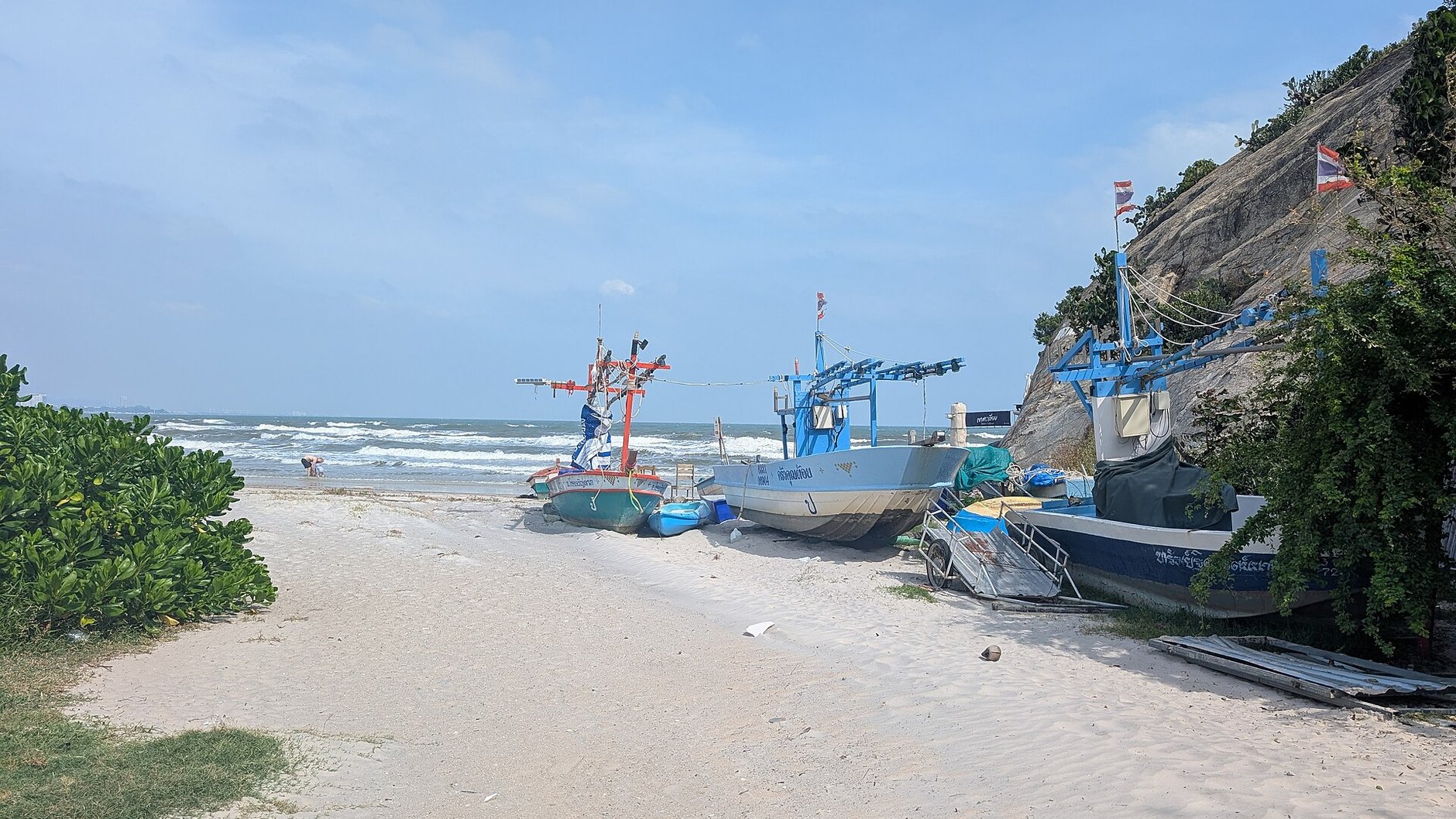 Fishing boats pulled up on a sandy Hua Hin beach beside a rocky headland (illustrative stock photo)