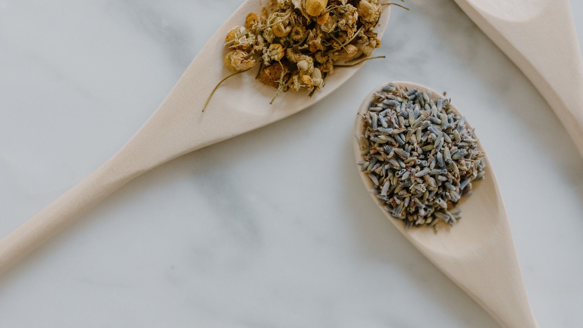 Dried chamomile and lavender heaped in wooden spoons on white marble (illustrative stock photo)